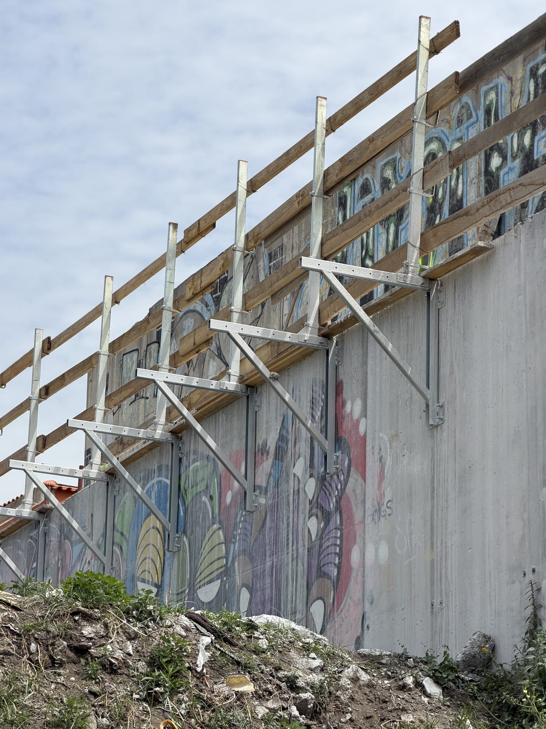 Alto muro della spalla in calcestruzzo con mensole in acciaio a sbalzo e parapetto provvisorio in legno
