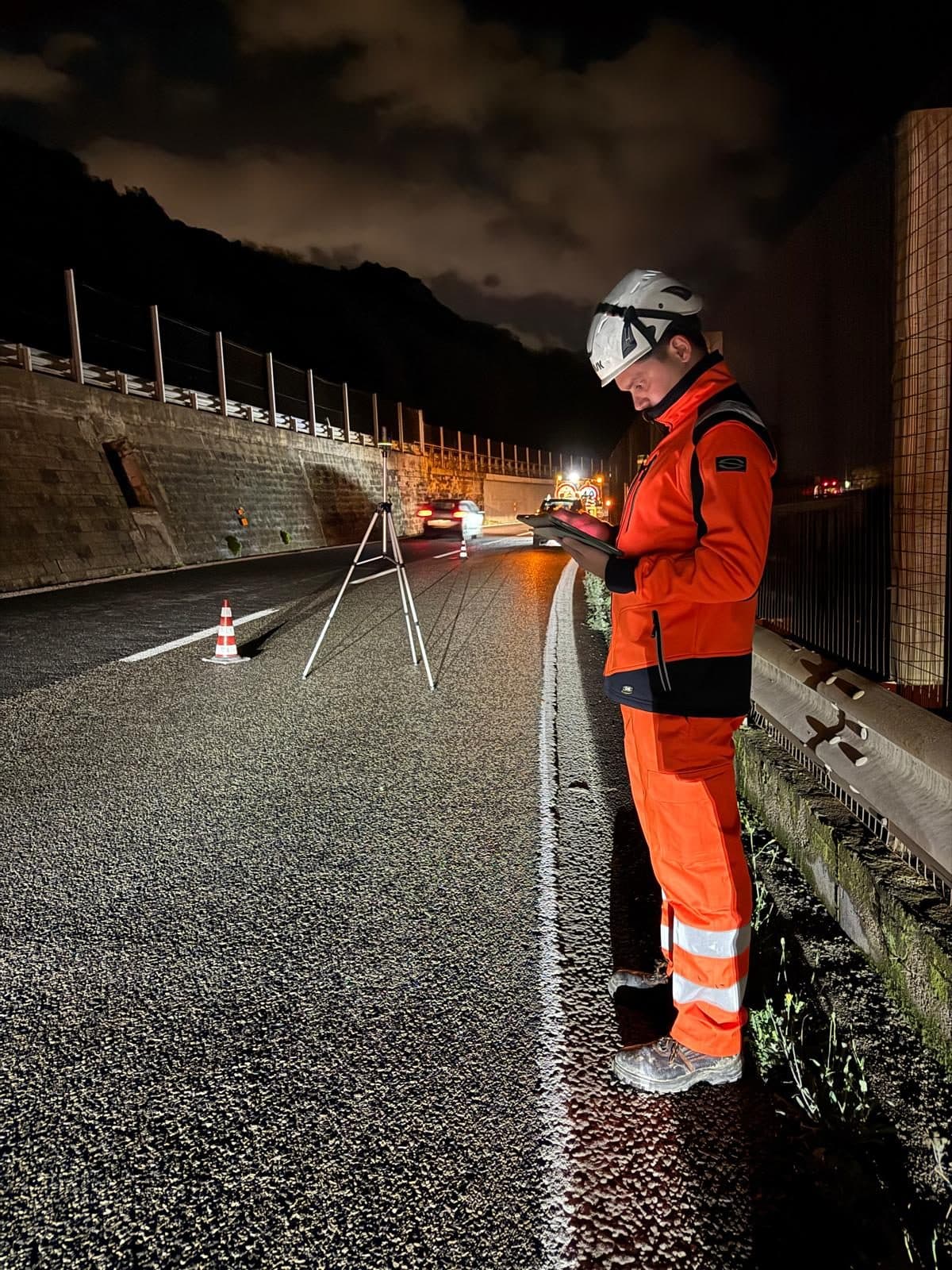 Tecnico con un tablet accanto al laser scanner sulla carreggiata, di notte